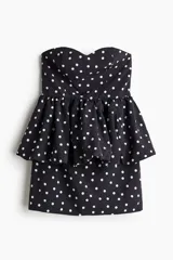 Vestido corto negro con estampado de lunares blancos. Diseño strapless con escote corazón y peplum superpuesto con efecto globo en la cintura.