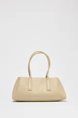 Bolso tipo tote color beige, con doble asa corta y cierre superior con botón imantado. Incluye un compartimento interno con cierre de cremallera.