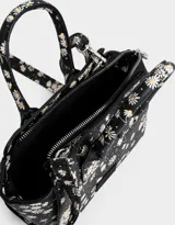 Cartera mini city de cuerina negra estampada con flores blancas. Tiene correa desmontable y doble asa corta.