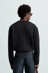 Jersey negro de corte boxy fit, tejido en hilatura con mezcla de algodón y 13% de cashmere. Tiene cuello redondo, manga larga y acabados en rib.