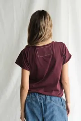 Remera de manga corta color bordó oscuro, con cuello redondo y dobladillos deshilachados en mangas y ruedo. Estampado frontal en blanco con el logo de la banda Queen y el texto "AMERICAN TOUR '77".