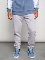 Pantalón de jogging gris claro, corte clásico, con logo de la marca Umbro bordado en negro en el muslo izquierdo y costuras en contraste.