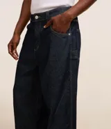 Pantalón de jeans azul oscuro, corte amplio tipo skater, con cintura con trabillas, cierre tradicional, bolsillos y costuras contrastantes.