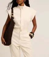 Mono largo color crema de sarga de algodón con elastano, cuello alto con botón, sin mangas, bolsillos laterales y trabillas en la cintura.