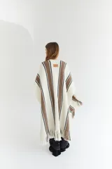 Ruana artesanal color beige con rayas horizontales rojas y amarillas, y flecos en el borde inferior.