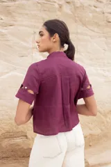 Blusa color camel con cuello mao, cierre frontal con botones y aberturas geométricas en hombros, mangas y cintura.