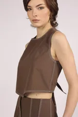 Blusa corta color marrón, sin mangas, con cuello redondo y pespuntes en contraste color blanco.