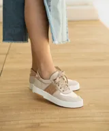 Zapatilla de cuero color tostado con detalles dorados y suela blanca.