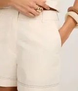 Short de tiro alto color beige confeccionado en algodón con lino, con trabillas en la cintura, cierre tradicional, bolsillos delanteros y costuras aparentes.