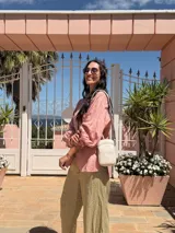 Bandolera pequeña tipo 'phone bag' de símil cuero color rosado pálido, con cierre de cremallera y correa ancha de tela con diseño de chevron en tonos claros.