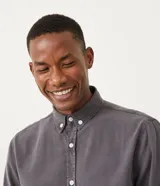 Camisa de hombre de manga larga, color gris oscuro, corte clásico, con cuello abotonado y cierre frontal con botones blancos.