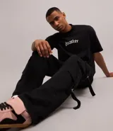 Pantalón cargo recto color negro, de sarga de algodón, con bolsillos laterales con hebillas y trabillas en la cintura.