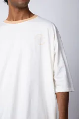 Remera color arena con manga corta negra, cuello redondo con ribete negro y estampado pequeño en el pecho con la frase "Don't worry be happy".