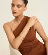 Brazaletes rígidos dorados en kit de dos unidades. Incluye un brazalete cerrado de diseño liso y un brazalete abierto tipo cuff con terminaciones decorativas en forma de hoja y un cristal artificial.