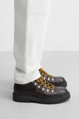 Bota de cuero color marrón oscuro con cordones amarillos, estilo trekking, con suela de goma con volumen.