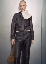Chaqueta bomber de cuero color marrón oscuro con cuello camisero y cierre frontal con cremallera y botones a presión. Tiene terminaciones elásticas en puños y cintura, y dos bolsillos laterales.