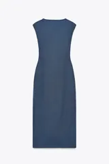 Vestido midi color beige, de corte recto, con escote en pico cruzado, sin mangas y detalle de hebilla metálica en la cintura.