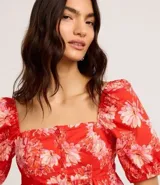 Blusa peplum cropped de tricolina con estampa floral, escote cuadrado, mangas abullonadas cortas y botones delanteros.