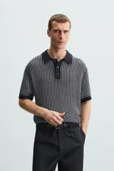 Polo de hombre de corte relajado, tejido de punto de algodón a rayas verticales en tonos gris y negro. Tiene cuello solapa, cierre frontal con botones y mangas cortas.