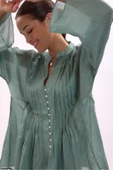 Camisa verde agua con cuello mao, abotonada al frente y mangas largas acampanadas con detalle de pinzas verticales en el frente.