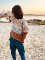Sweater de lana merino color tostado, con cuello redondo y mangas largas. Presenta un diseño geométrico con motivos étnicos en tonos beige, azul y naranja.