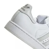 Zapatillas Adidas Superstar blancas con las tres tiras laterales en gris claro y puntera de goma.