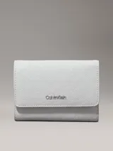Billetera de plegado triple Calvin Klein, color blanco o gris muy claro, con textura de monograma en relieve y logo metálico plateado en el frente.