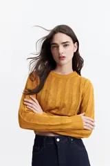Sweater de punto color mostaza, con diseño de ochos y textura calada. Tiene cuello redondo, mangas largas y terminaciones acanaladas en puños y cintura.