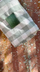 Necessaire rectangular de tela estampada a cuadros verdes y blancos, con cierre superior y etiqueta verde con logo.