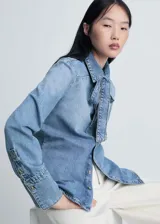 Camisa de jean celeste con cuello camisero y lazo al cuello, de manga larga con puños abotonados y corte recto.