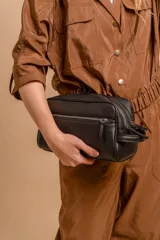 Neceser unisex de símil cuero color camel, con forma rectangular y asa lateral. Presenta un bolsillo frontal con cierre vertical y un compartimento principal con cierre superior.