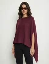Poncho tejido de punto, color vino tinto, con cuello redondo y abertura en los laterales para los brazos. Presenta un dobladillo asimétrico.