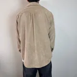 Sobrecamisa color beige de pana con cuello clásico, cierre con botones y bolsillo de parche en el pecho. Corte recto y mangas largas con puños abotonados.