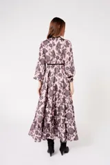 Vestido largo rosado con estampado floral negro, escote en V con ribete negro, mangas largas abullonadas y falda escalonada con volantes.