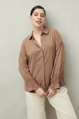 Camisa negra de manga larga con cuello clásico y botones frontales. El tejido presenta una textura arrugada o plisada, y los puños tienen un detalle fruncido o elástico.