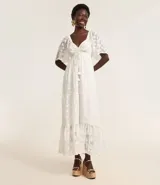 Vestido largo evasé de crepé blanco con textura y volados. Tiene escote corazón, elástico en la cintura, lazo con cordón y borla en las puntas, y mangas cortas.