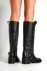 Bota de cuero negra de caña alta con hebillas y apliques metálicos.