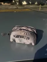 Neceser gris de tela satinada con cierre superior y detalle de moño en el frente.