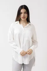 Camisa blanca de lino, de corte holgado, con cuello clásico, cierre frontal con botones, bolsillo en el pecho y mangas largas con puños abotonados.