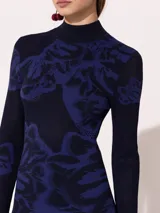 Vestido midi ajustado al cuerpo, de punto calado con estampado floral en azul y negro, cuello alto y volados en puños y ruedo.