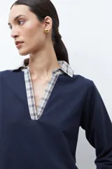 Sweatshirt azul marino de manga larga con cuello en V, superpuesto a una camisa de cuadros beige y azul que asoma en el cuello, puños y ruedo.