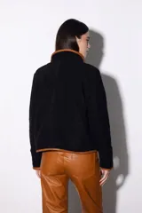 Chaqueta corta de paño a cuadros en tonos beige y negro, con cuello mao y ribete de cuero marrón en todo el contorno. Se ata con lazos de cuero en el centro y tiene bolsillos laterales.