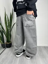 Pantalón baggy gris con bolsillos laterales y traseros. Estampado con la palabra "Gangster" en el bolsillo trasero.