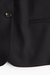 Blazer negro de botonadura sencilla con solapas de muesca, bolsillo superior insertado y bolsillos delanteros. Modelo con hombreras, botonadura frontal, botón decorativo en los puños y abertura atrás.