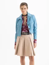 Chaqueta corta de cuero ovino color celeste claro, con cuello solapa, botones forrados y bolsillos aplicados en el frente. Las mangas presentan recortes y forma curvada.