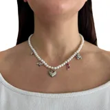 Collar corto de perlas pequeñas con dijes de metal plateado y zirconia: corazón, abeja, zapato de tacón, oso de peluche y copo de nieve. Cierre de mosquetón con cadena para regular el largo.