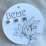 Arete en forma de flor con piedras brillantes, disponible en varios colores.