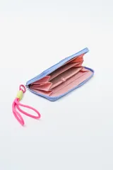 Billetera rectangular color fucsia con cierre perimetral y parche frontal negro con logo. Incluye correa de mano de cordón rosa neón y detalle de ajuste en verde lima.