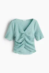 Top color celeste con textura arrugada, escote en V, mangas cortas y frunces en el delantero y los laterales.