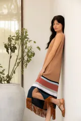 Vestido tejido en hilado de algodón con flecos de gamuza color tostado, con rayas horizontales en el ruedo en tonos negro, blanco, ladrillo y celeste.